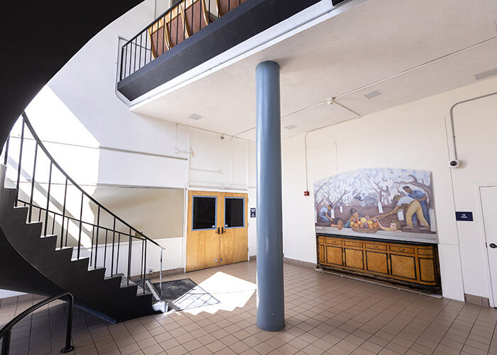 The curving central staircase in Stern Hall is shown leading down to a wall mural.