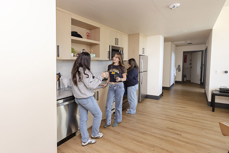 Three students stand and talk to each other near the kitchen counter of an Anchor House apartment.