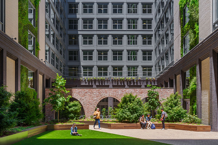 Several people are shown in the central courtyard between buildings. There are many trees within the courtyard.