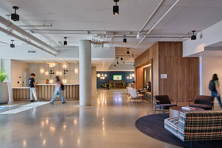 An employee sits behind the front desk of the lobby. The front desk area leads to a large space with many smaller lounge areas nestled within it.